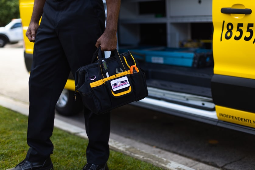 One Hour Heating & Air technician walking away from company van carrying a stocked toolbag in his hand.